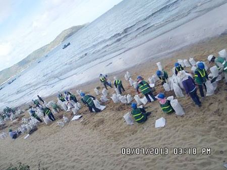 Environment workers collect layers of oil from the beach on July 8 (Photo: SGGP)